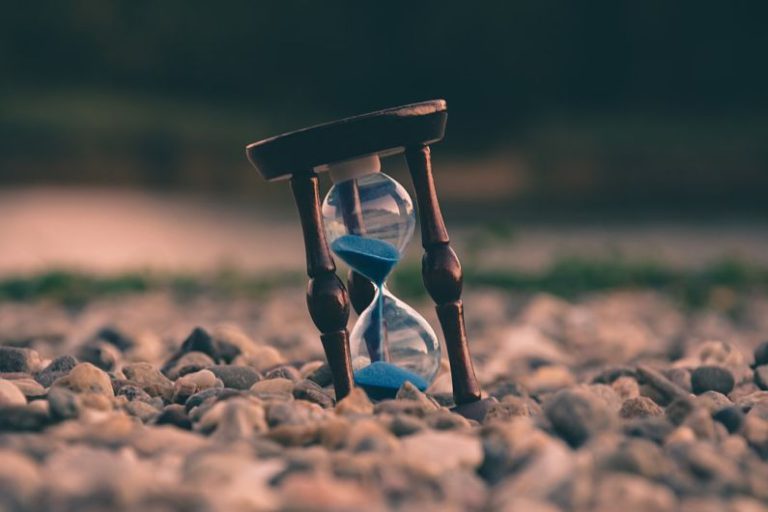 Time - selective focus photo of brown and blue hourglass on stones